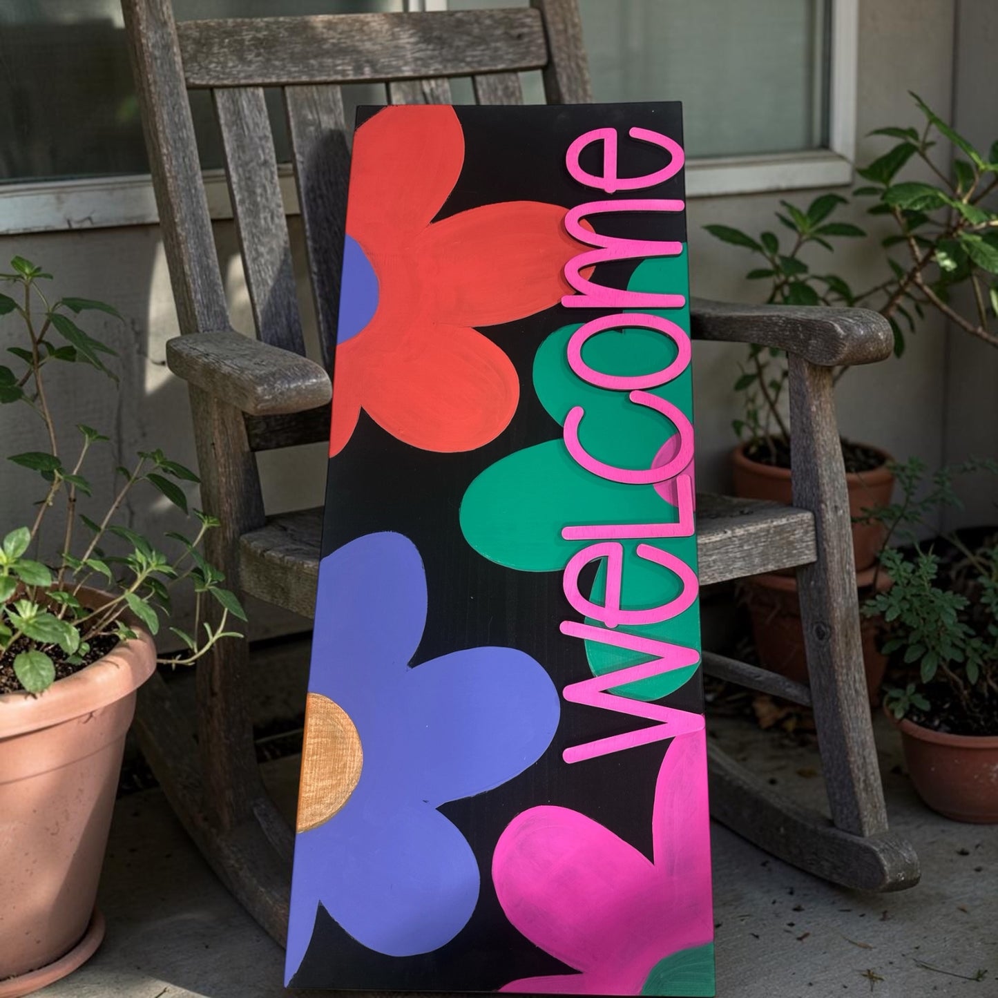 Colorful 'Welcome' sign with abstract shapes on a wooden chair outdoors.