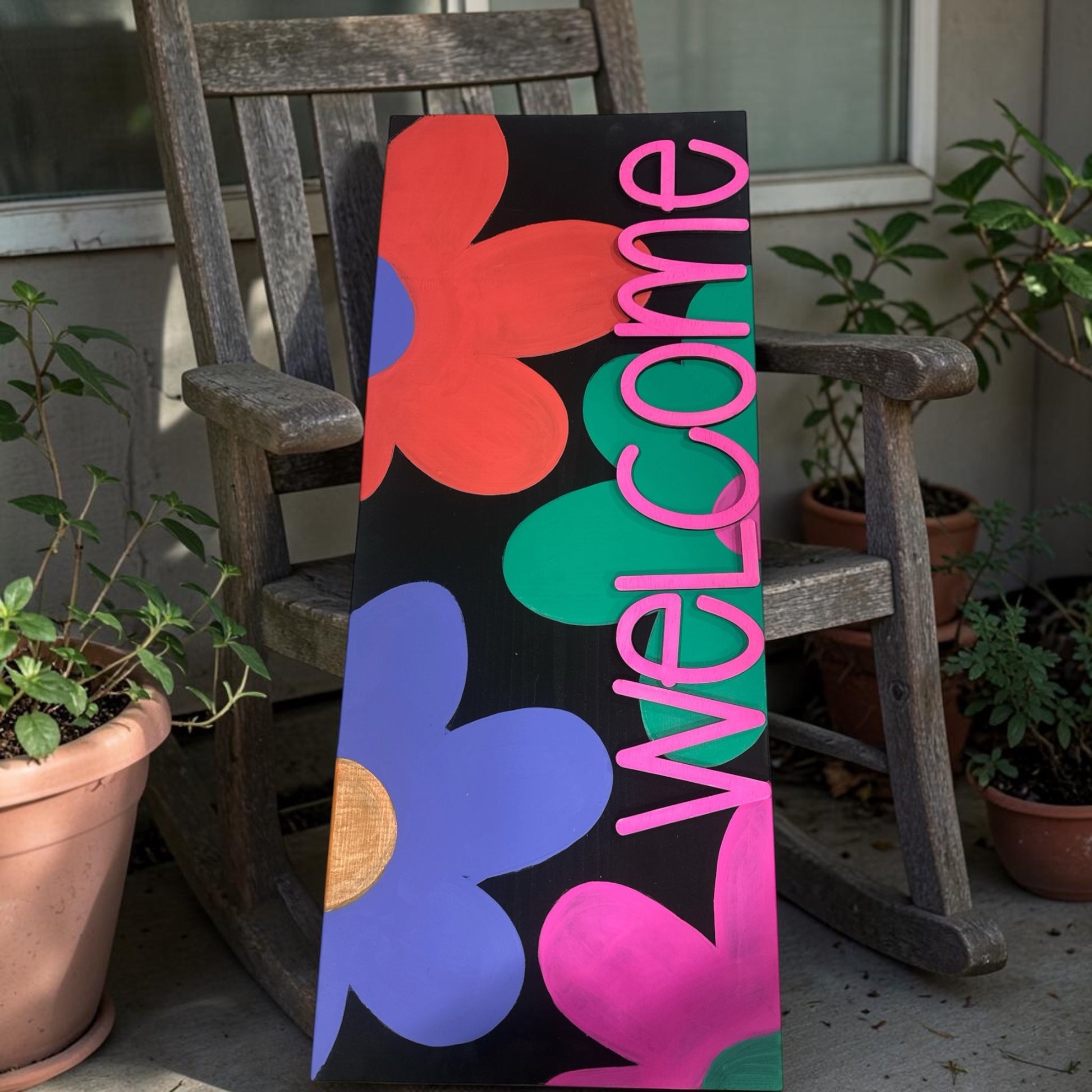Colorful 'Welcome' sign with abstract shapes on a wooden chair outdoors.
