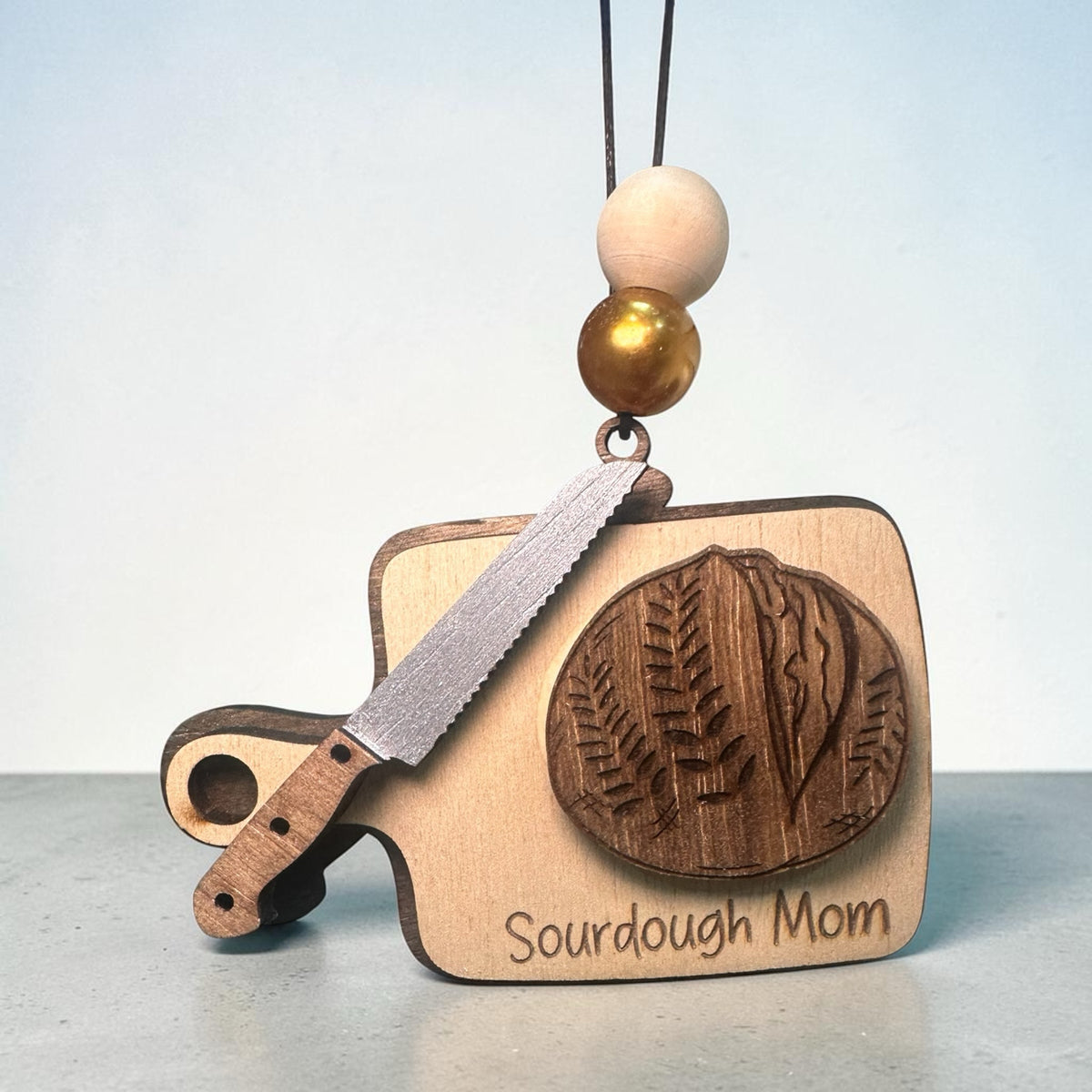 Squiggle Laser and Design Sourdough Mom wooden hanging ornament featuring a cutting board, bread knife, and loaf.