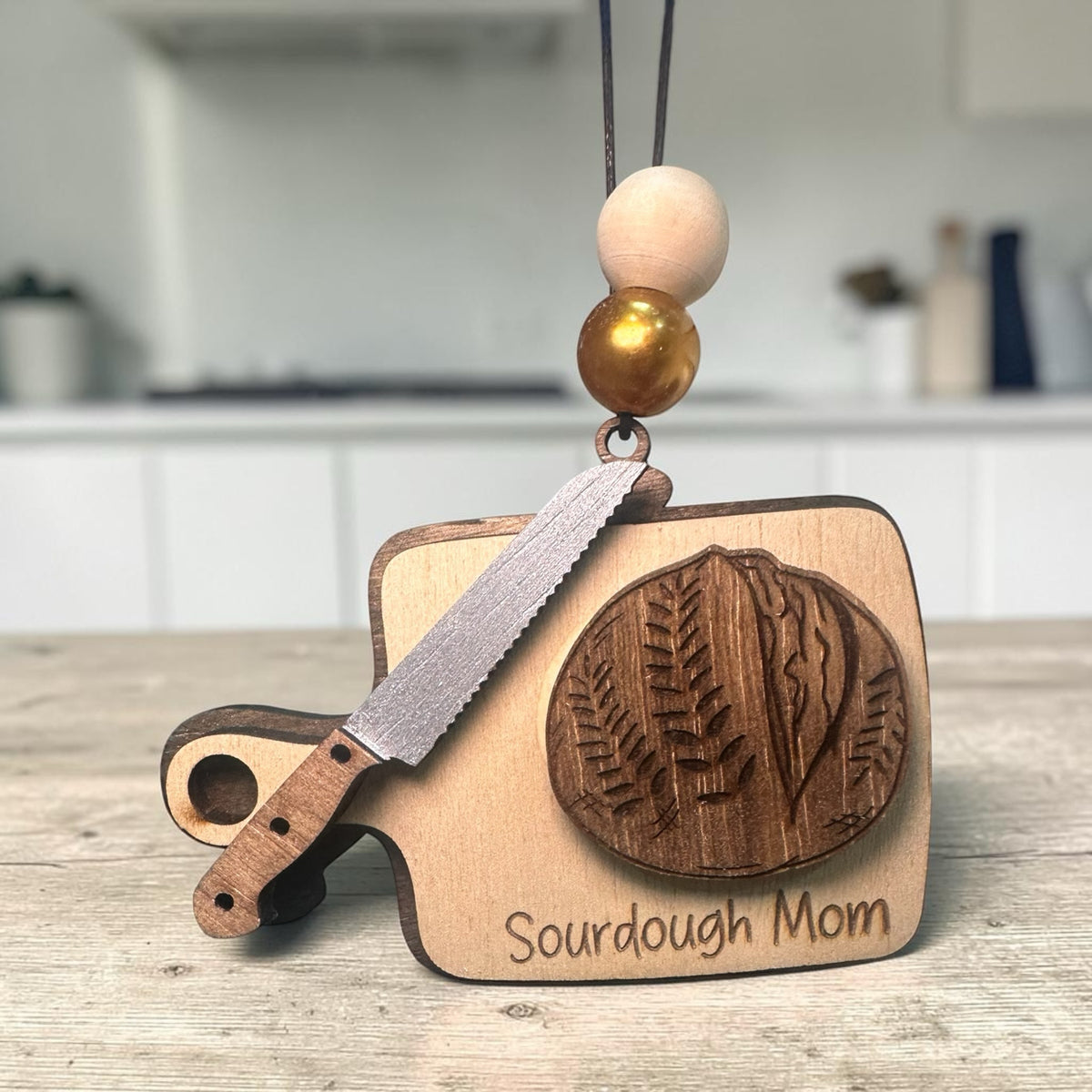 Squiggle Laser and Design wooden Sourdough Mom ornament with bread knife and loaf design, featuring gold-toned beads.