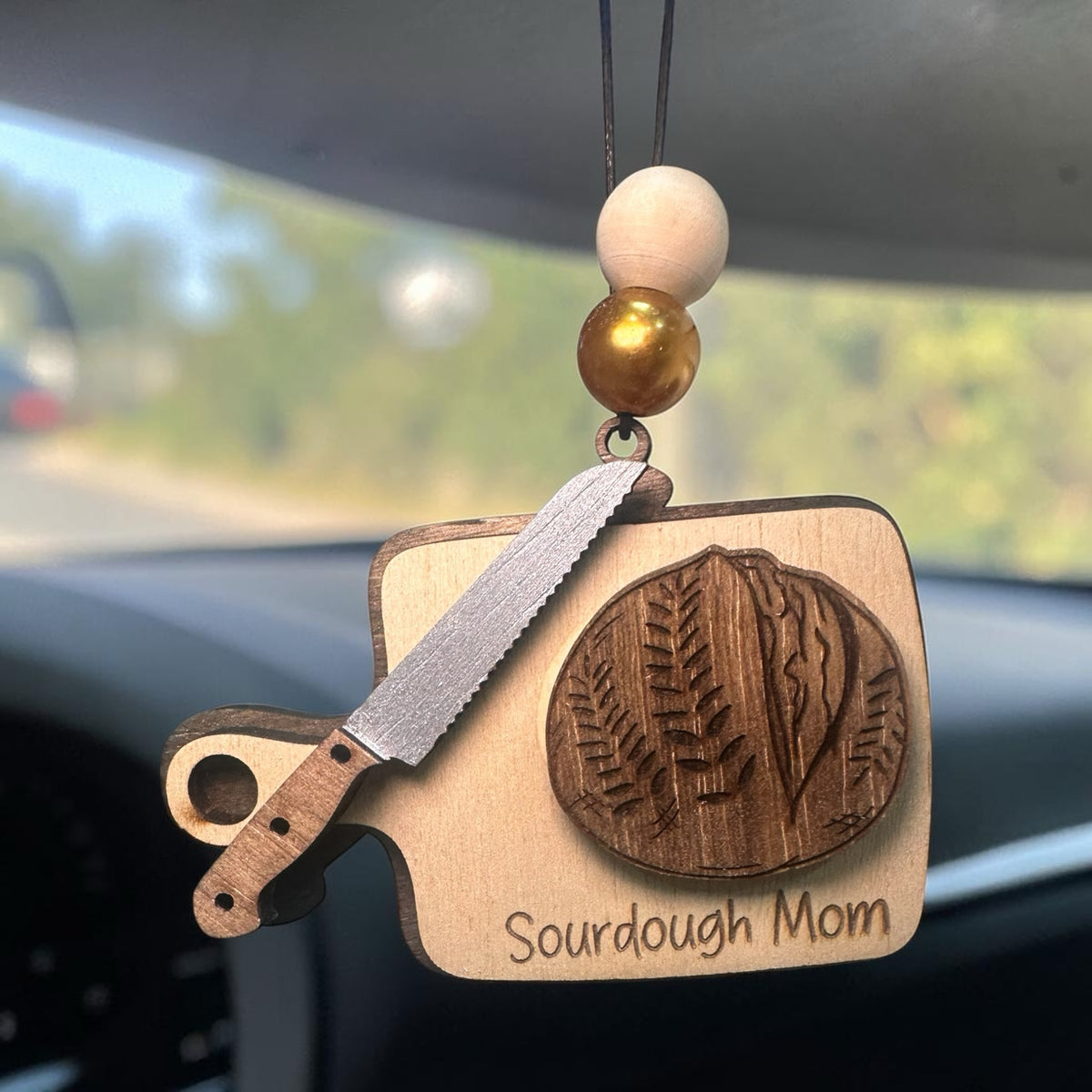 Squiggle Laser and Design wooden Sourdough Mom ornament with bread knife and loaf design hanging in a car